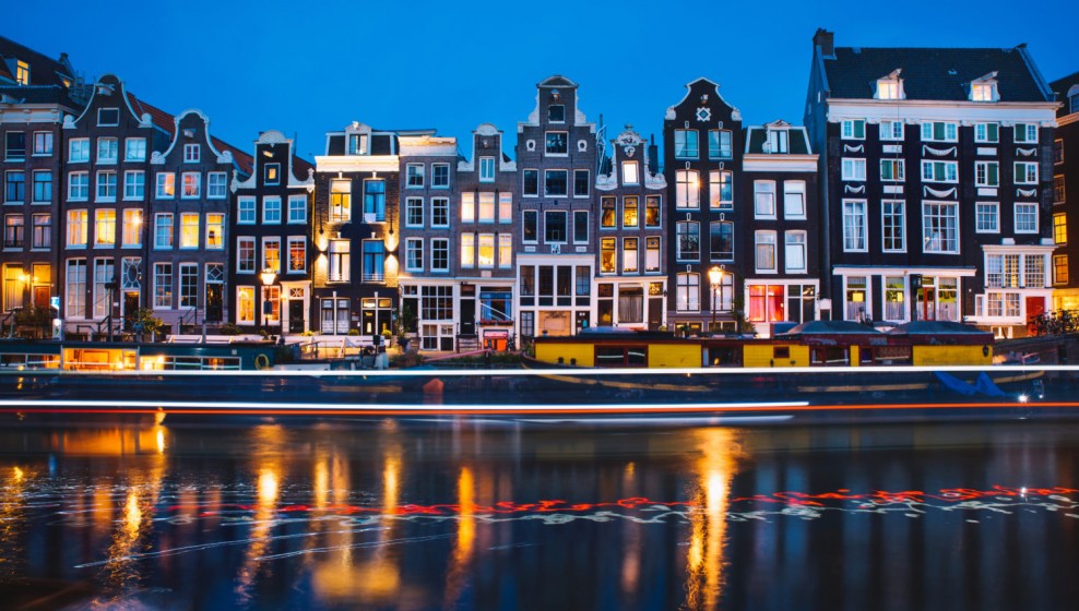 Amsterdam canal with boats and dutch houses at night.